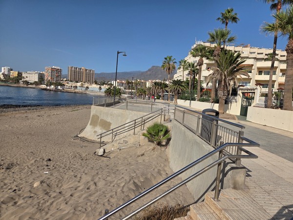 Concrete access ramp with metal railings leading from the promenade down to the sand at Playa de Los Tarajales in Los Cristianos.