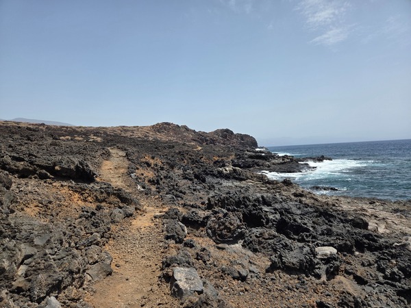 Narrow coastal trail cut through jagged lava along the Malpaís de Güímar shoreline.