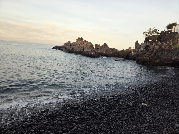 Pebble beach of Playa Méndez near Alcalá with rounded volcanic stones and jagged lava formations enclosing the cove.