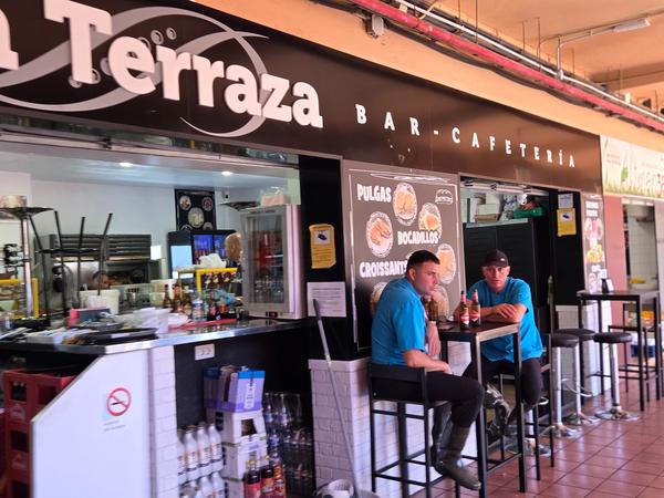 Dos trabajadores sentados frente a una cafetería en el interior del mercado.