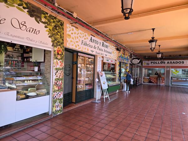 Tiendas de pasta artesanal, dulces y pollos asados alineadas en un pasillo del mercado.