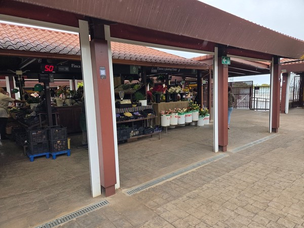 Close view of produce counters and a flower stall under tiled roof pavilions.