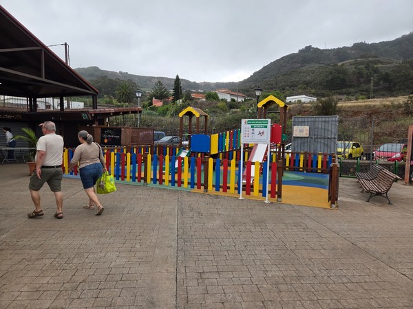 Fenced children’s playground with colorful equipment next to the market pavilions.