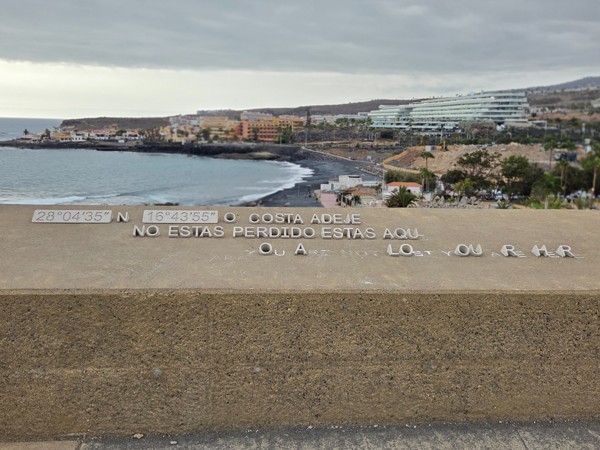 Stone parapet at the Mirador de las Palomas inscribed with the coordinates of Costa Adeje and the phrase ‘You are here’, overlooking the bay.