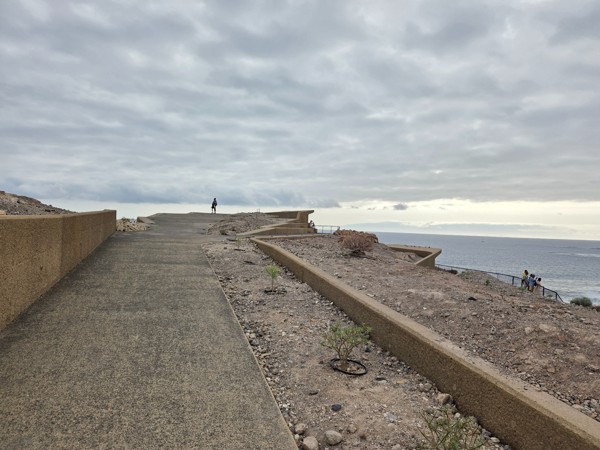 Smooth paved walkway at the Mirador de las Palomas with low protective walls, leading toward the lip of the cliff above the Atlantic.
