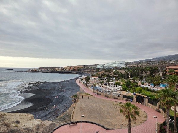 Wide coastal panorama from Mirador de las Palomas, with the black-sand beach, curved promenade and resorts of Costa Adeje in the background.
