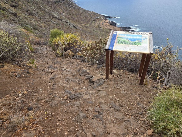 Interpretive panel about the Costa de Acentejo on the cliff path with the coastline descending to the sea.