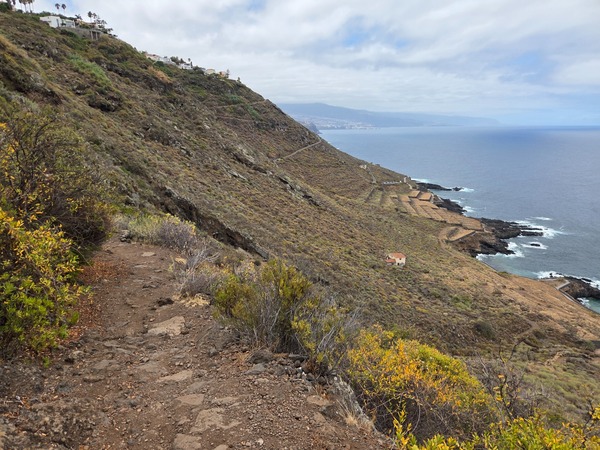 View down to the rocky headland and pathways at the base of the cliff, with waves breaking around the promontory.