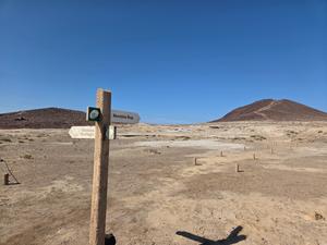 Trail signs in the dry landscape pointing toward Montaña Roja and Montaña Bocinegro.