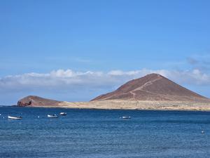 View from the upper slope of Montaña Roja with volcanic soil and scattered vegetation overlooking the sea.