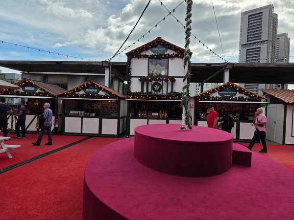 Row of Christmas market stalls in front of tall buildings at El Corte Inglés in Tenerife with a central circular platform on the red carpet.