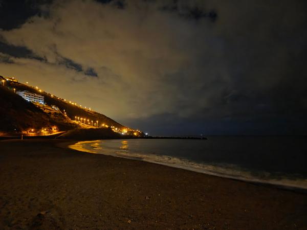 Night view of Playa de La Nea with orange street lights illuminating the hillside and beach promenade.