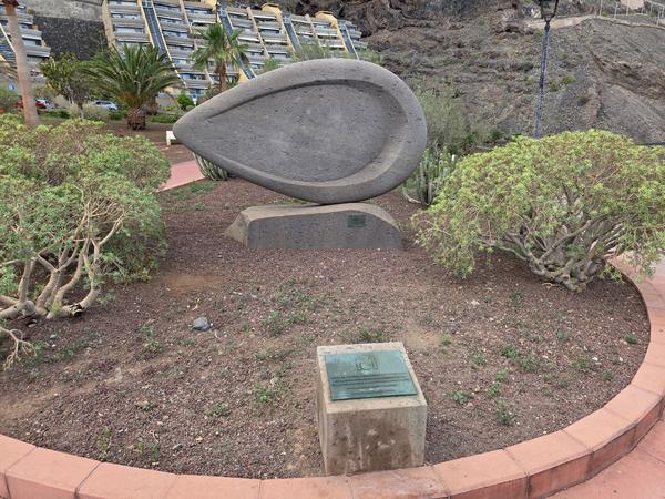 Modern volcanic stone sculpture near the promenade at Playa de La Nea, surrounded by desert plants.