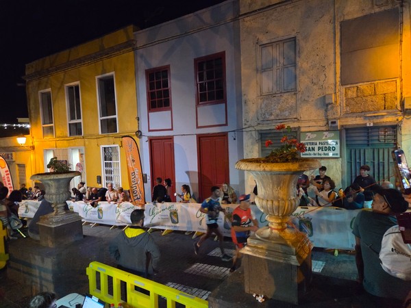 Runners passing fast in front of colourful houses while spectators clap and watch La Nocturna Güímarera race.