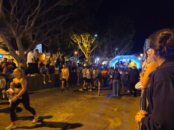 Groups of people in race shirts and casual clothes chatting and enjoying the festive atmosphere of La Nocturna Güímarera.