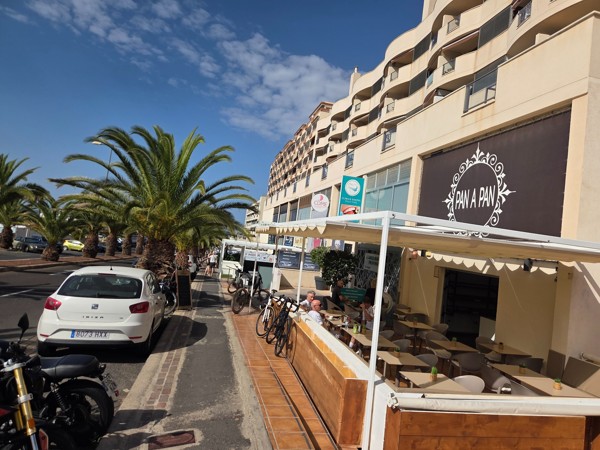 Terrace of the Pan a Pan café in Palm-Mar with people sitting at tables along a palm-lined street.