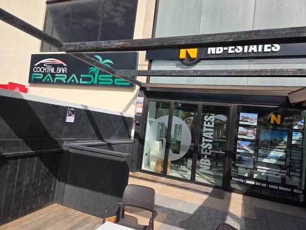 NB-Estates real estate office in Palm-Mar next to Cocktail Bar Paradise with property photos displayed in the windows.