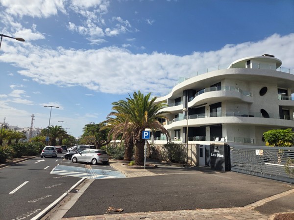 Curved modern building of Residencial Las Olas in Palm-Mar with large balconies and a palm-lined street in front.