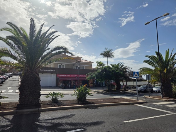 Supermarket and small commercial strip in Palm-Mar under the Terrazas del Faro complex with palm trees around the parking area.