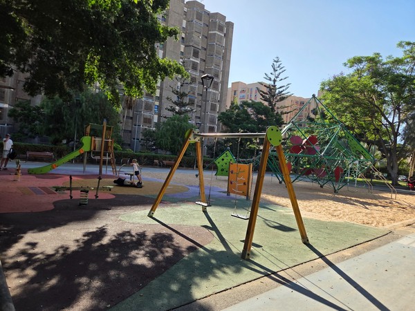 Family play zone with slides, swings and spring riders next to the rope-climbing nets, all shaded by mature trees.