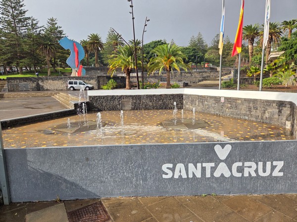 Entrance fountain at Parque La Granja with the white heart Santa Cruz logo, flags and a colourful sculpture behind.