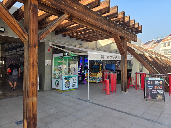 Outdoor terrace of the Flipper arcade area at Pasarela Shopping Center with red bar stools, arcade machines and wooden beams overhead.