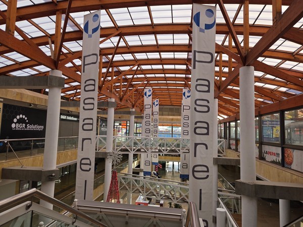 Interior view of Pasarela Shopping Center in Tenerife with tall banners hanging from the wooden roof and several shopfronts on different levels.