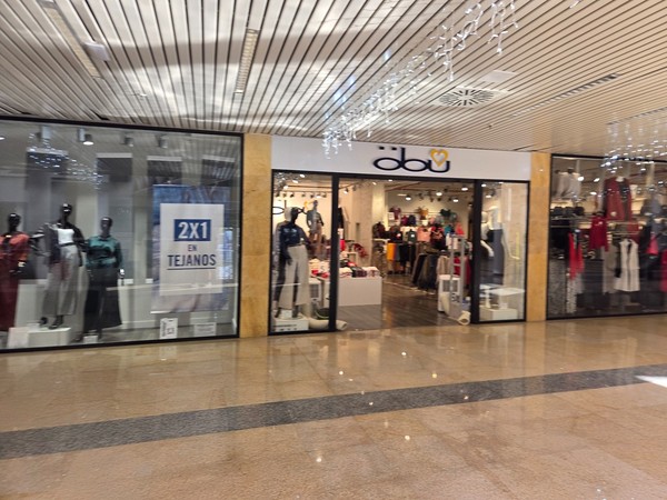 Fashion boutique inside Pasarela Shopping Center with mannequins in the window, a 2x1 on jeans promotion sign and clothing displays under warm lighting.