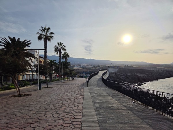 Wide seaside walkway at Playa San Juan with curved railing and stone paving facing the Atlantic at sunrise.