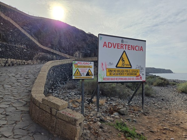 Warning signs at Playa Aguadulce advising about rockfall danger and the lack of lifeguard service.