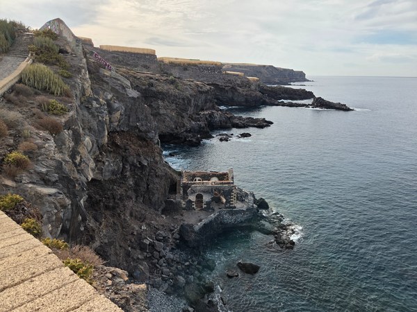 Old coastal structure with arches at the base of the Playa Aguadulce cliffs, surrounded by dark volcanic rock and clear water.