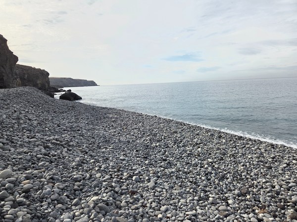Close view of rounded grey pebbles covering the beach at Playa Aguadulce beside gentle Atlantic waves.