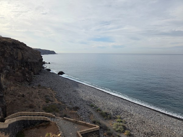 Long stretch of pebble shoreline at Playa Aguadulce with cliffs to the left and calm blue water.