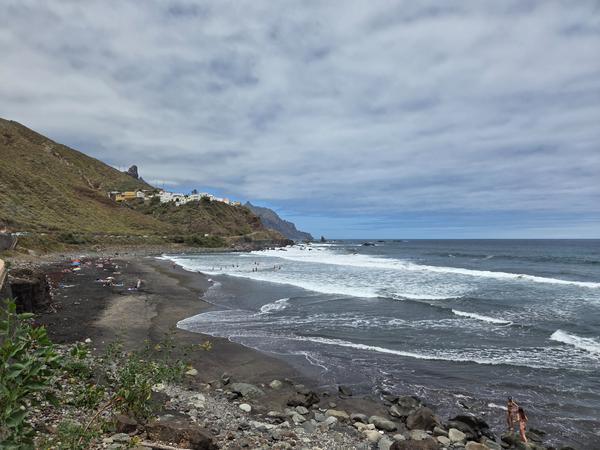 Wide expanse of black sand beach with small waves and bright skies.