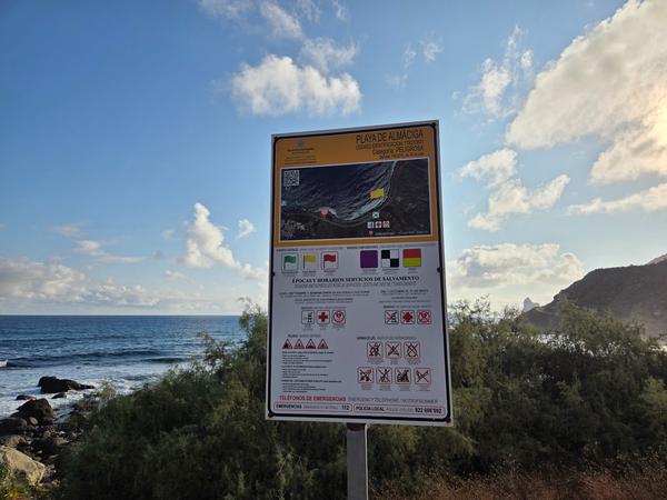 Official Playa de Almáciga sign with safety information and colored flags.