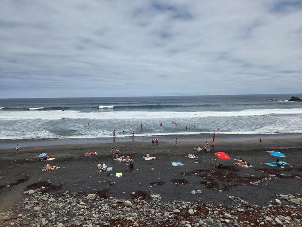 Groups of people swimming and relaxing along the shoreline of Almáciga beach.