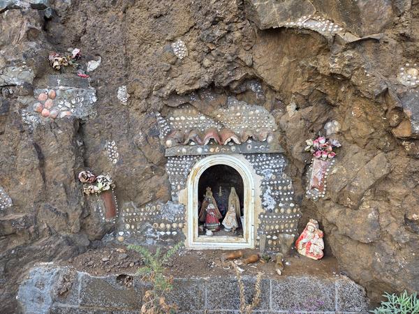 Small religious shrine with figurines and shells embedded in a cliffside near Almáciga.