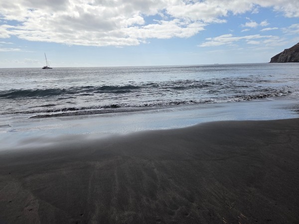 Wide stretch of black volcanic sand at Playa de Antequera with gentle waves rolling in under a cloudy sky.