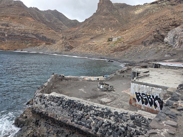 Small cluster of simple houses and shacks overlooking Playa de Antequera, built on terraces above the black sand beach and the calm sea.