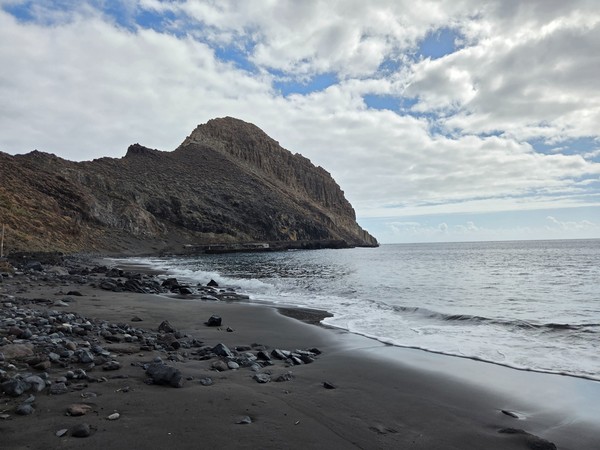 Layered volcanic and sandstone cliffs rising directly from the black sand at Playa de Antequera on the Anaga coast.