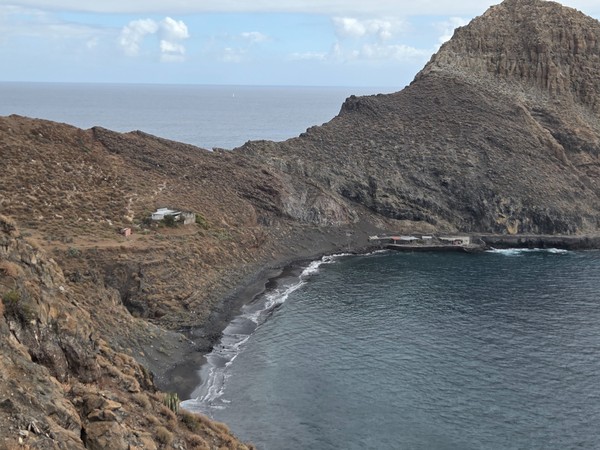 High viewpoint above Playa de Antequera showing the curve of the black sand beach, turquoise water and scattered simple houses on the surrounding slopes.