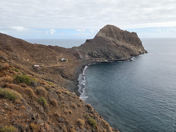 Wide panoramic view of Playa de Antequera bay in Tenerife, with steep volcanic cliffs enclosing a remote black sand beach and calm Atlantic waters below.