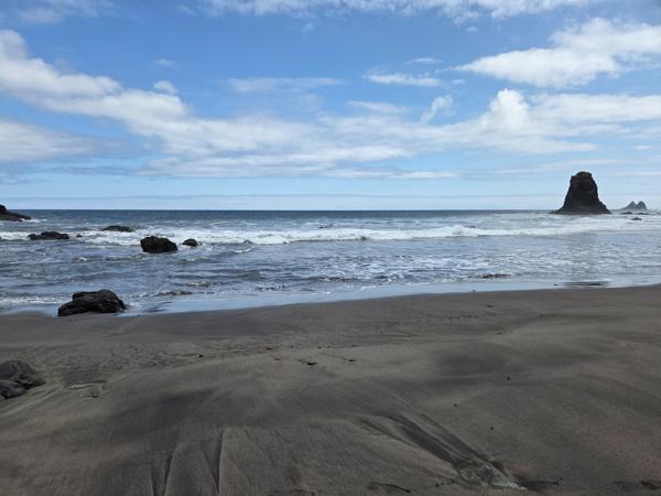 Smooth black sand on Playa de Benijo with gentle wave marks and sea stacks on the horizon.