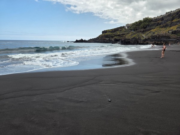 Close-up of Playa El Bollullo’s deep black sand and gentle shore break during calm seas.
