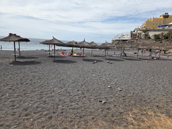 People relaxing on the black sand and swimming near the shore of Playa de Ajabo in Callao Salvaje.