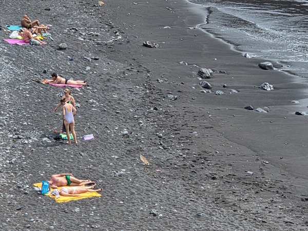 People sunbathing and wading along the black-sand shoreline of Playa de Ajabo.