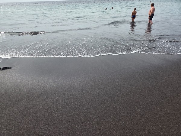 Close view of the compact black sand at the water’s edge on Playa de Ajabo with a small wave washing the shore.