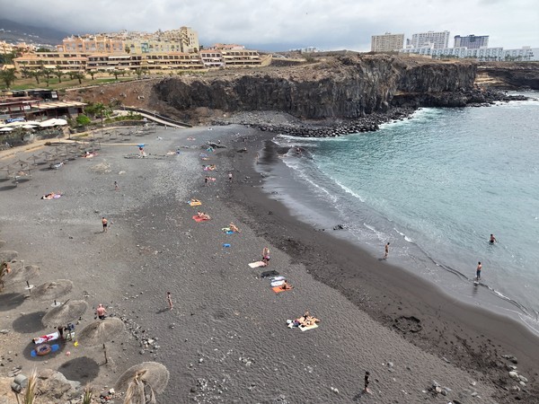 Wide panoramic view of Playa de Ajabo with the black-sand shoreline, breakwater and apartments of Callao Salvaje behind the bay.