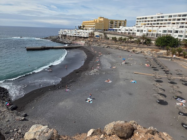 Clifftop vista of Playa de Ajabo showing the arc of black sand, calm water and the protective pier on the right side of the bay.