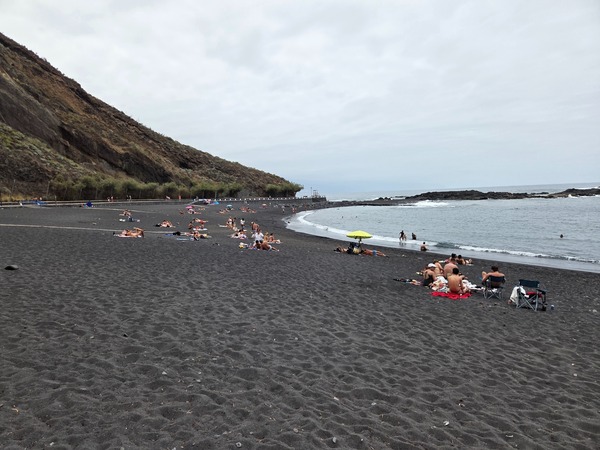Wide stretch of volcanic black sand at Playa de la Arena with calm Atlantic waves and sunbathers along the shoreline.
